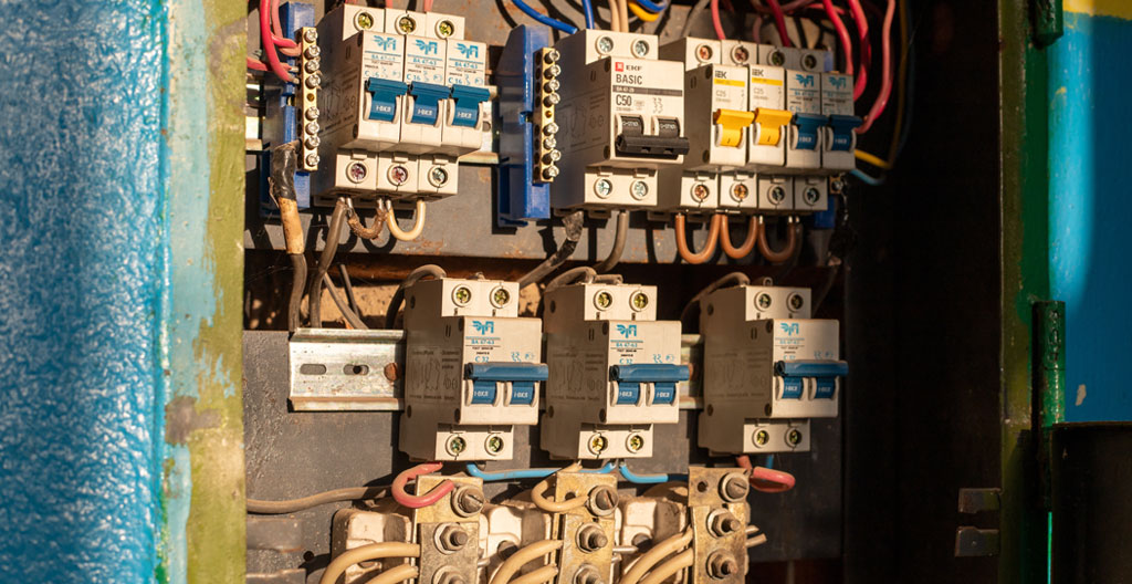 Mains d'une personne manipulant un tableau électrique ancien avec plusieurs disjoncteurs visibles